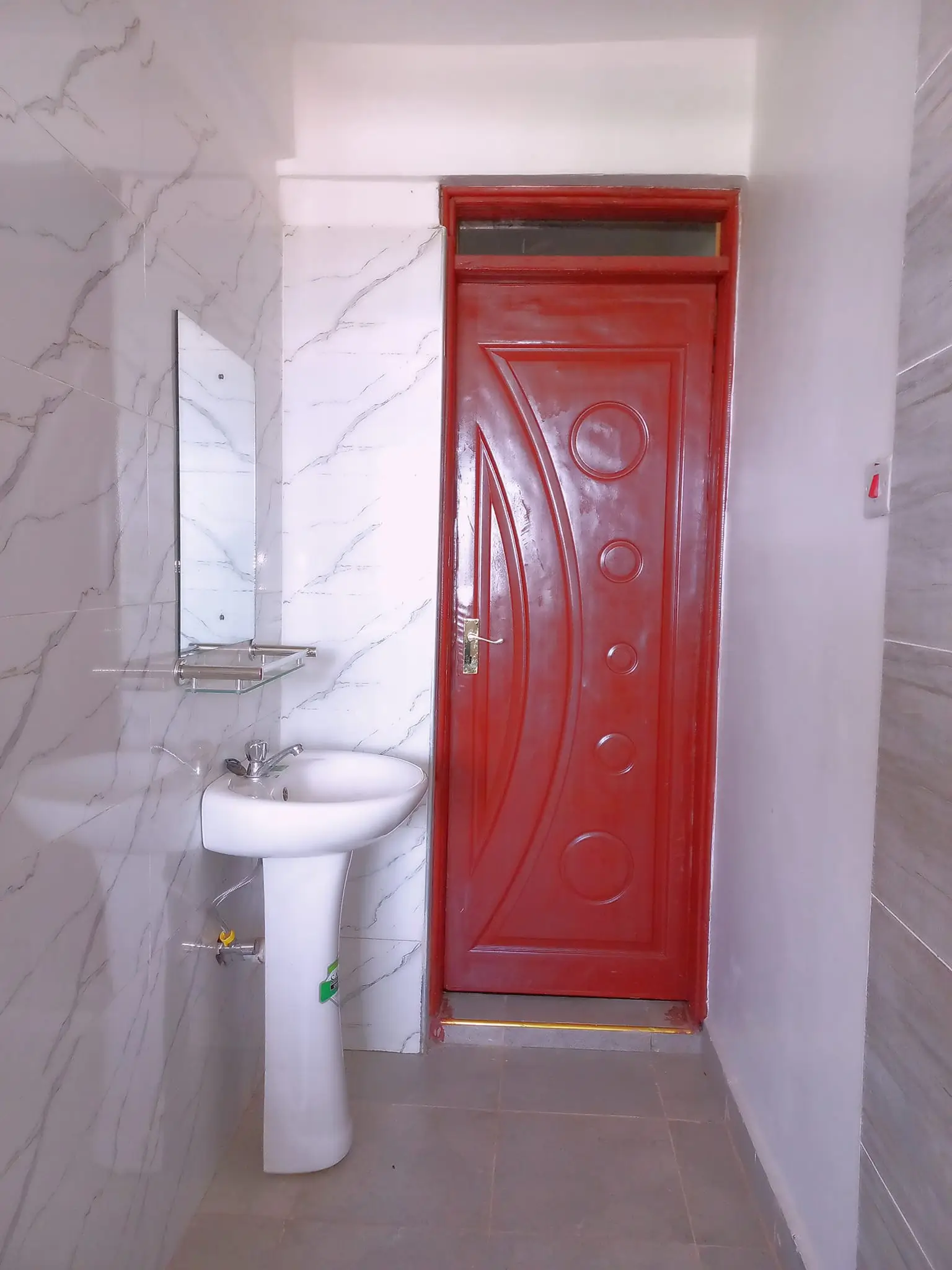 Compact bathroom with pedestal sink and red entrance door
