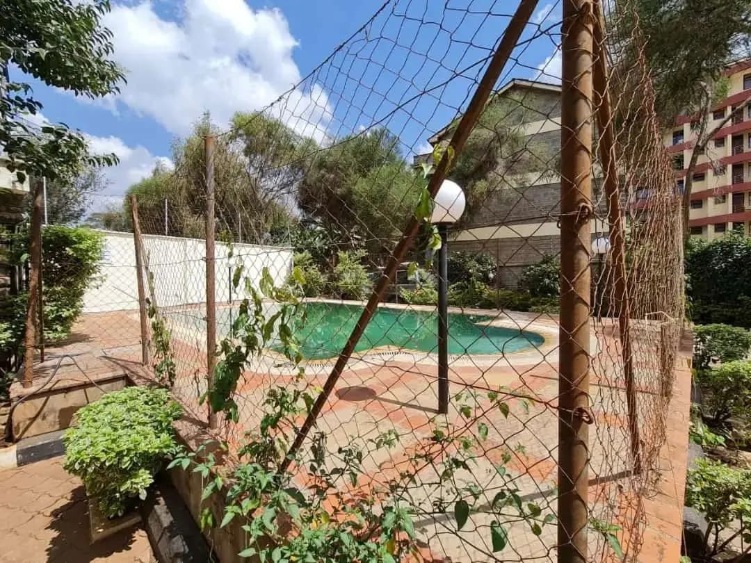 Swimming pool viewed through compound fencing with surrounding greenery