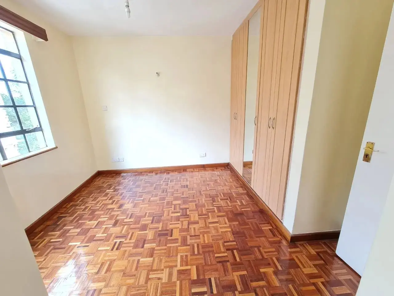 Spacious bedroom with herringbone wooden floor and built-in wardrobe