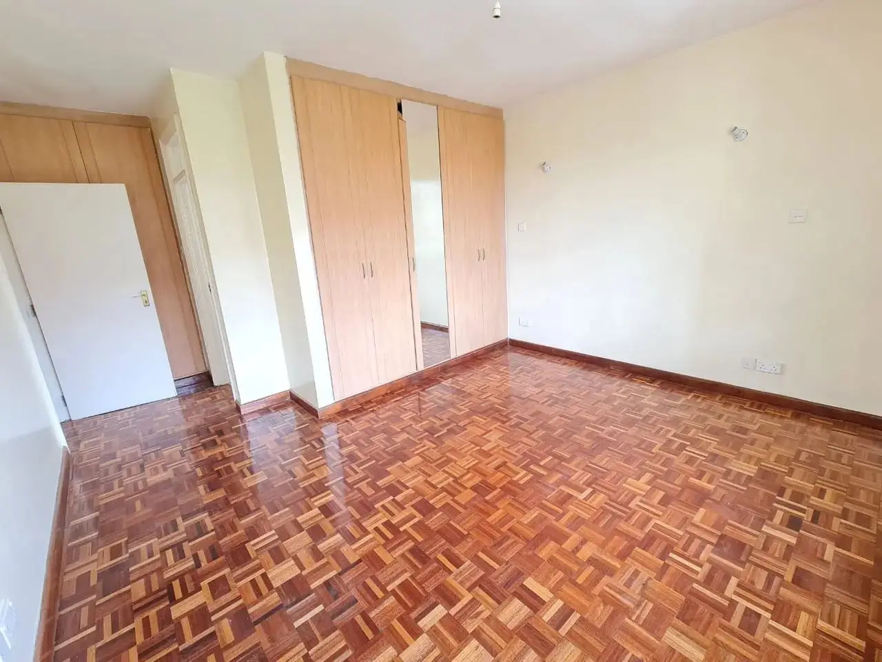 Spacious bedroom with herringbone parquet flooring and built-in wardrobes