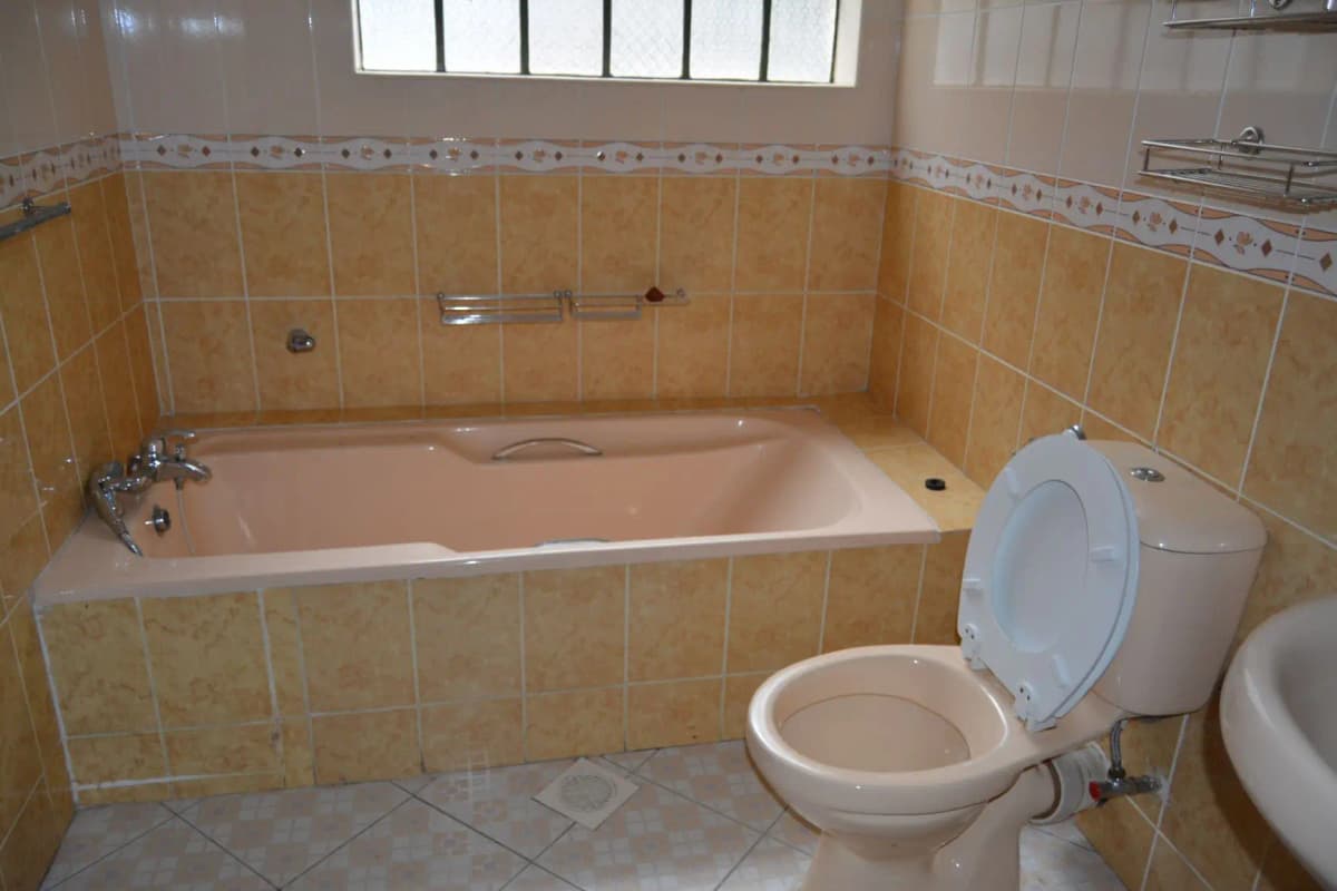 Spacious bathroom with bathtub, toilet, and beige tile walls