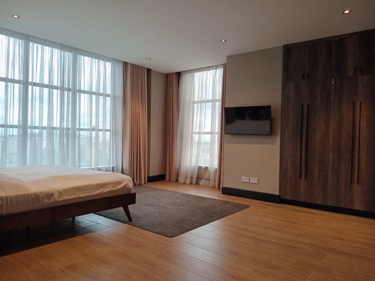 Spacious master bedroom with floor-to-ceiling windows and dark wood wardrobe