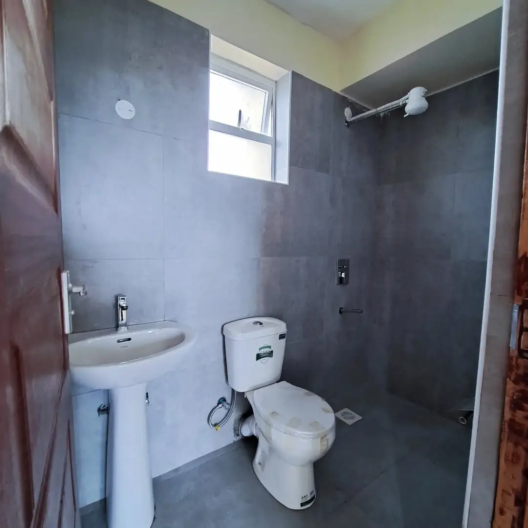 Modern bathroom with pedestal sink, toilet, and dark tile walls