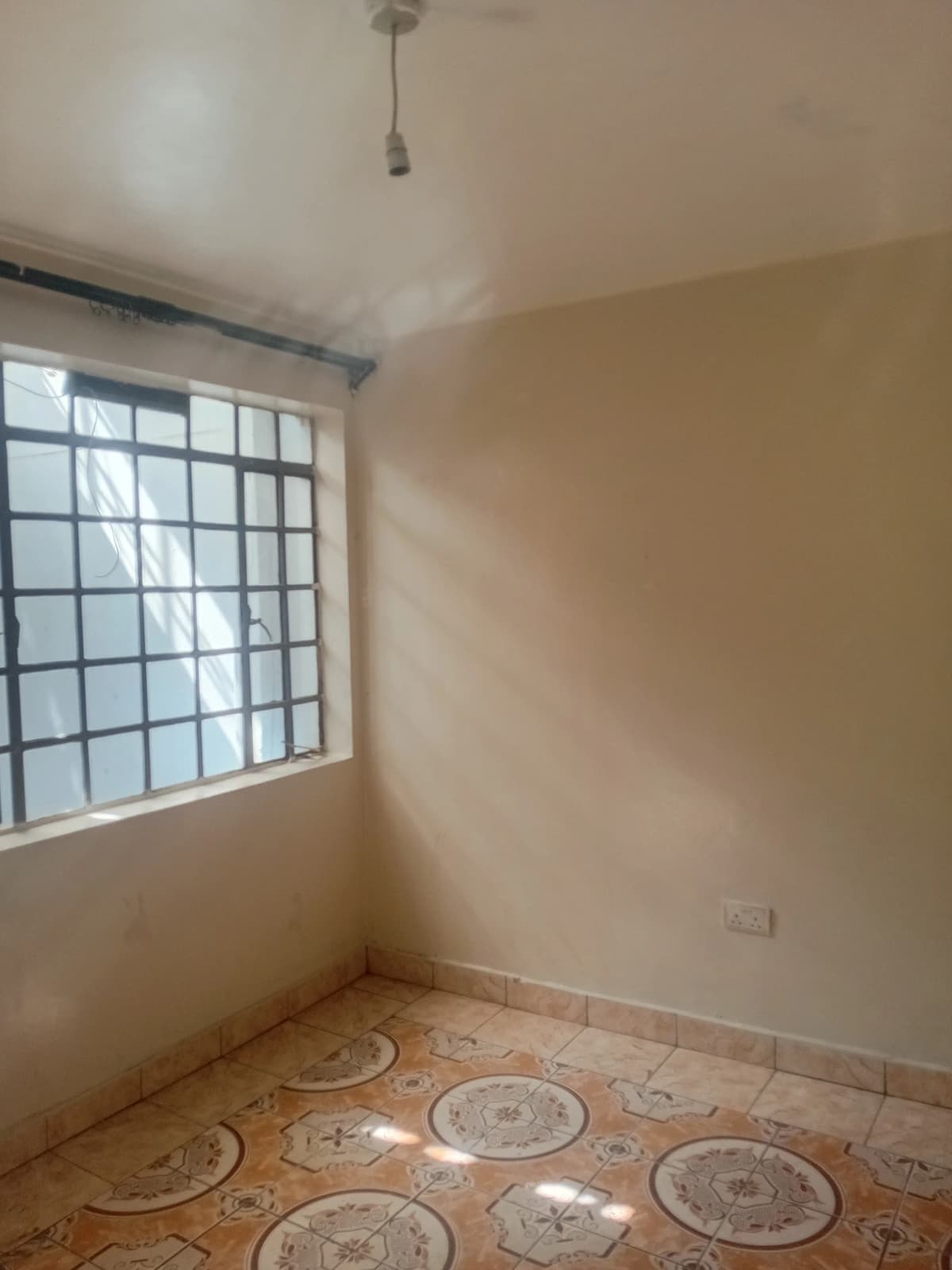 Unfurnished bedroom with barred window and decorative floor tiles