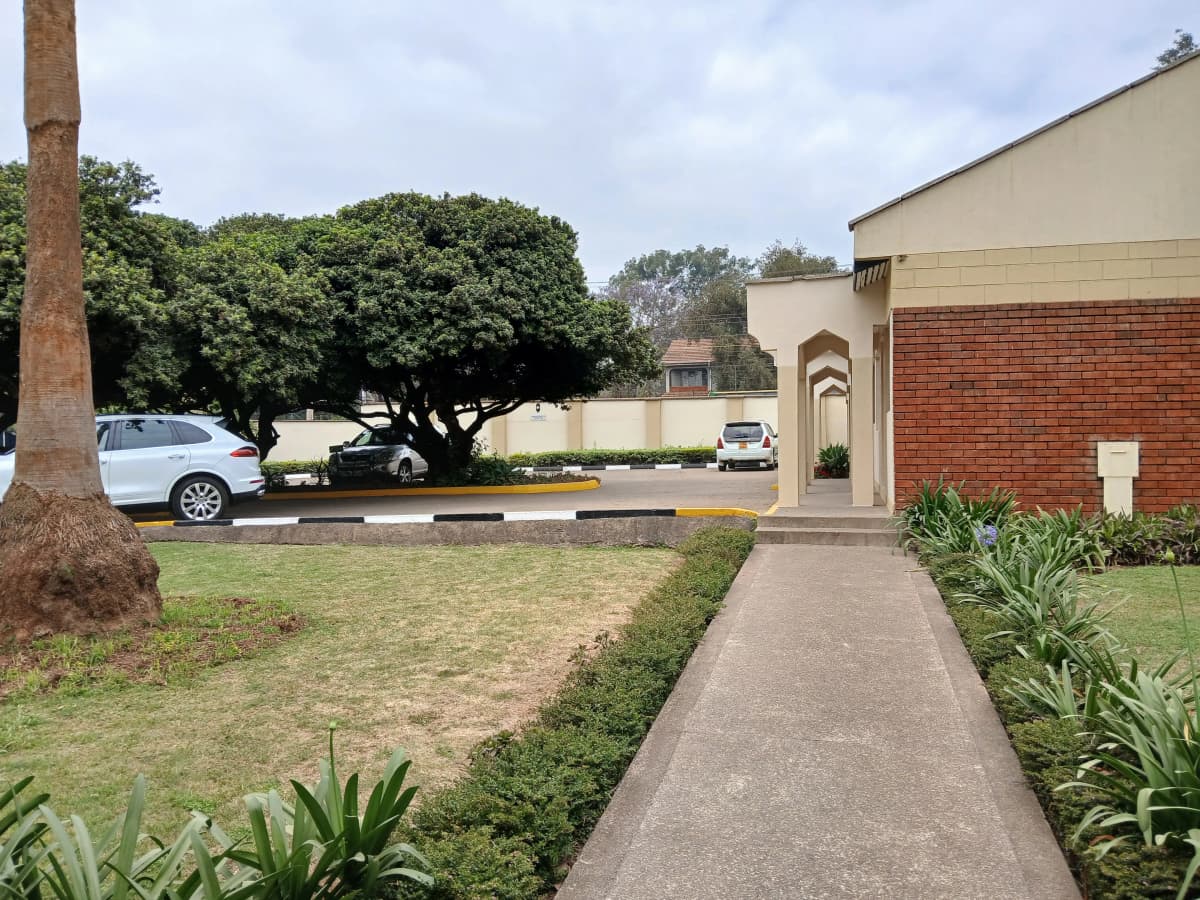 Property entrance with manicured lawn, driveway, and parked vehicles