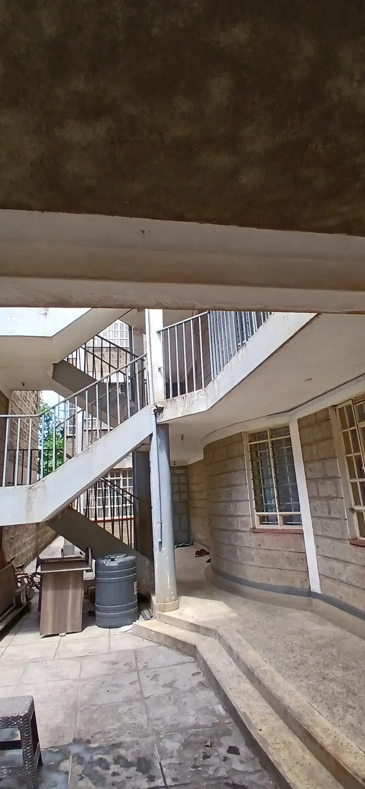 Exterior staircase with metal railing and paved compound area