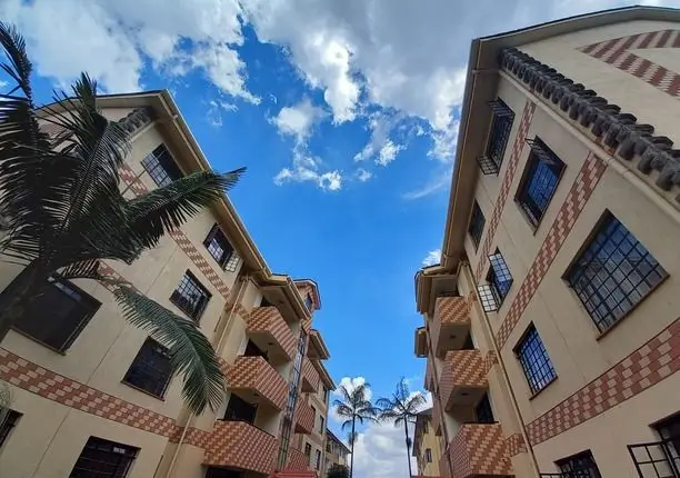 Multi-story residential building with red brick facade and palm tree