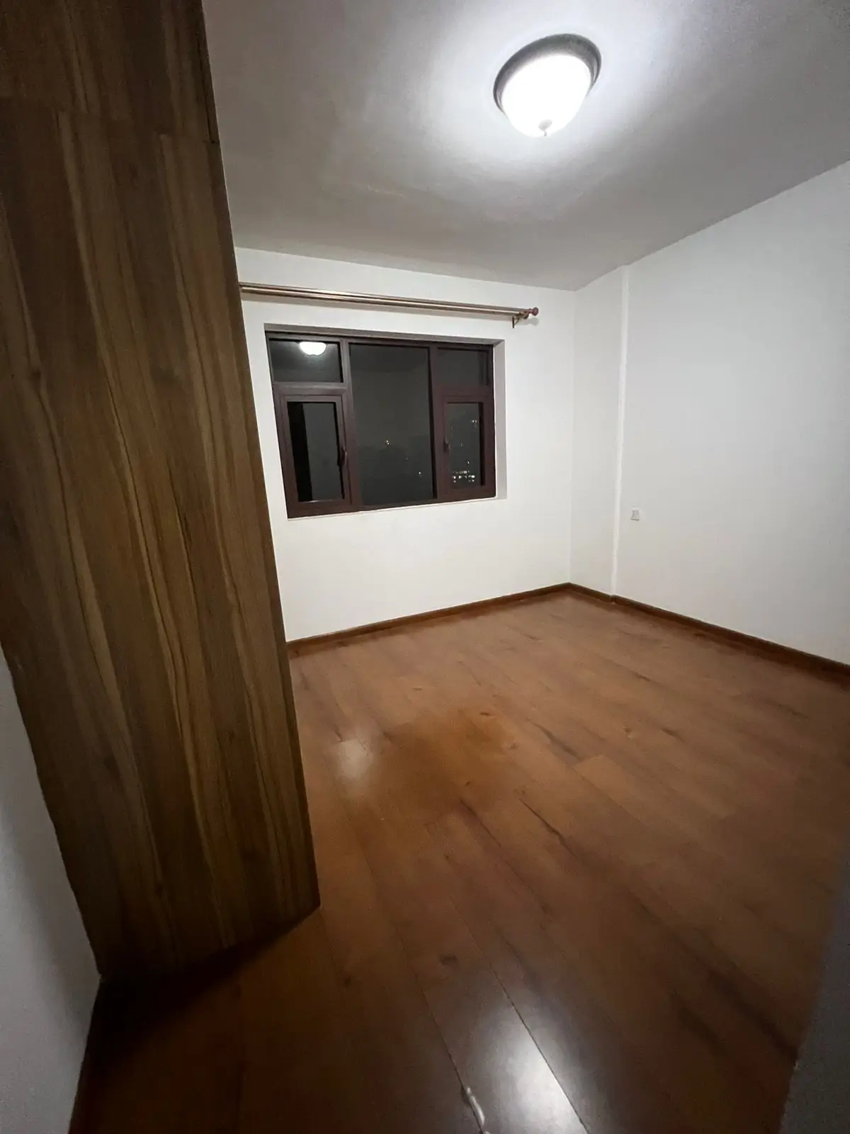 Empty bedroom with wooden flooring and window with curtain