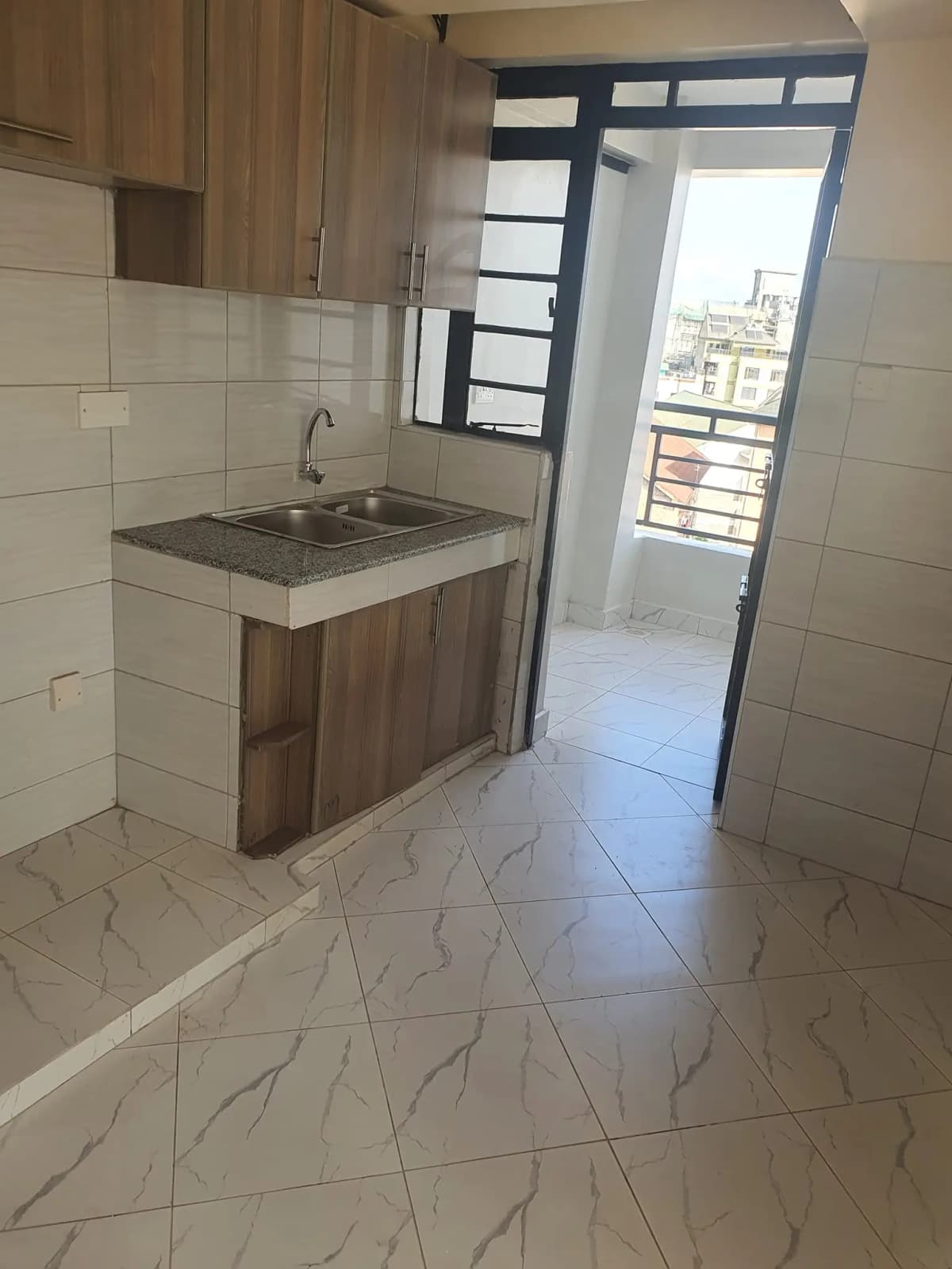 Compact kitchen with wooden cabinetry, sink, and balcony access