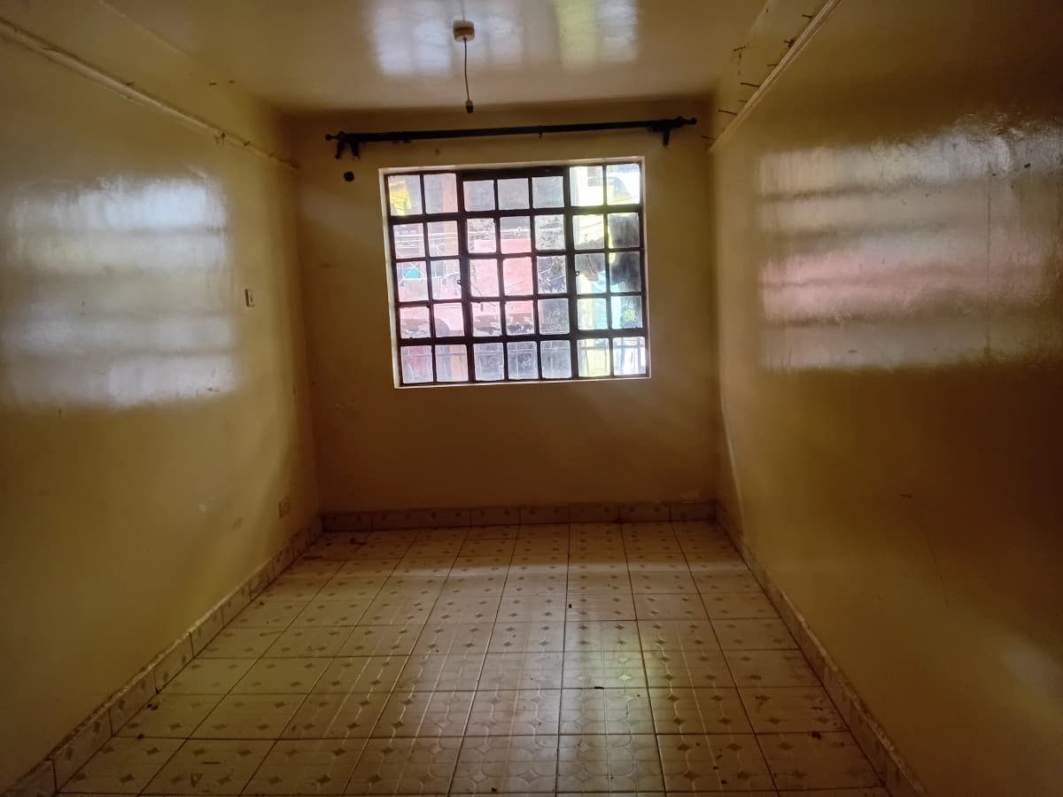 Empty bedroom with barred window and terracotta tile flooring