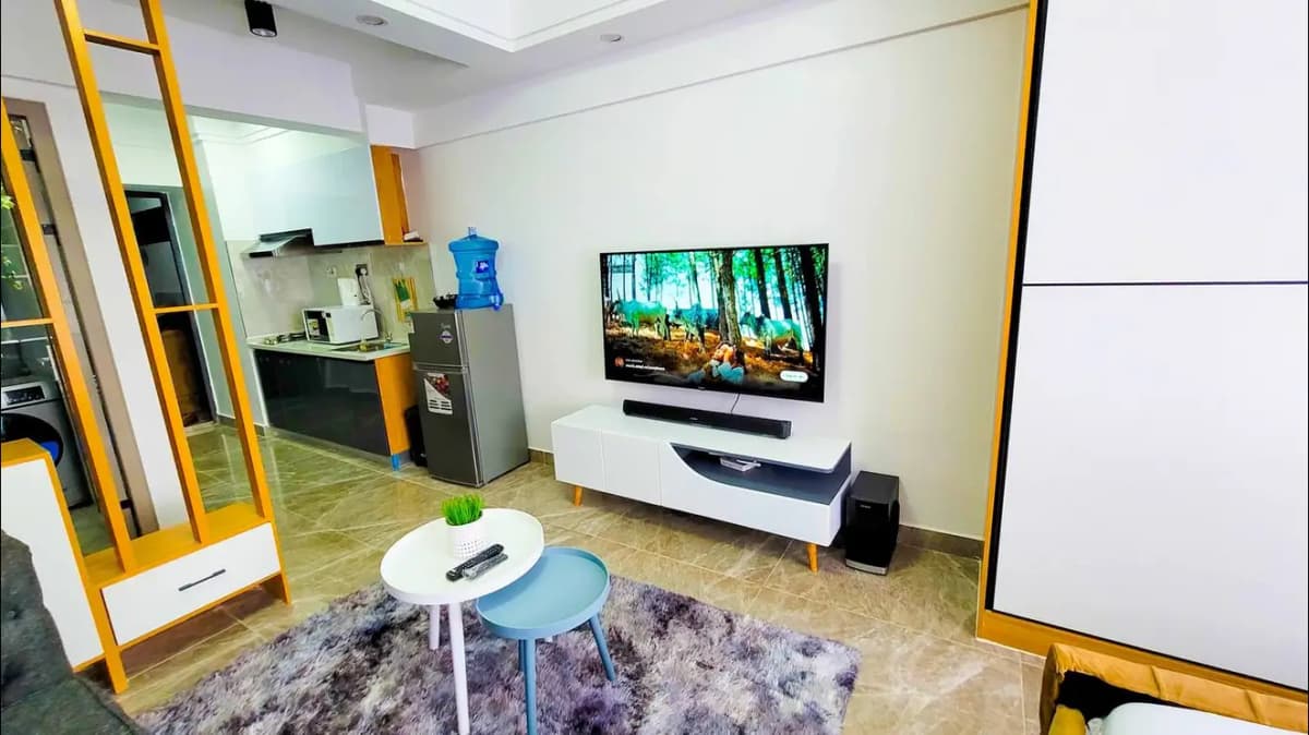 Modern open-plan living room with TV, kitchen visible beyond