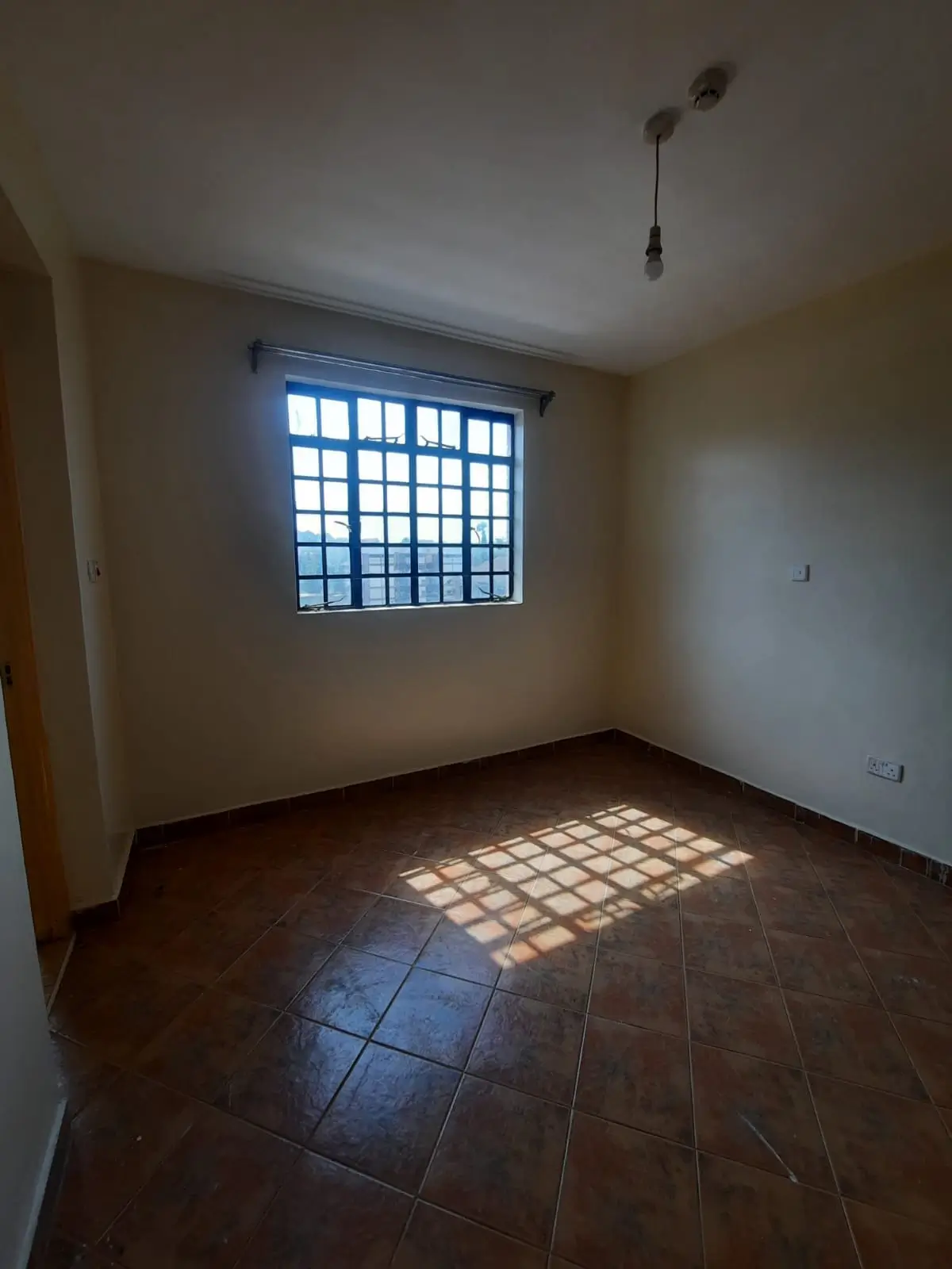 Bright bedroom with barred window and terracotta tile flooring