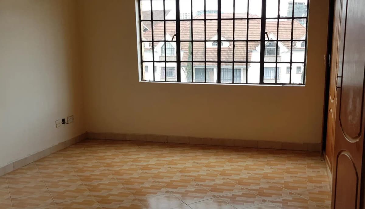Empty bedroom with barred window and wooden flooring