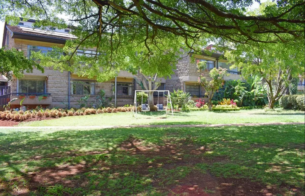 Manicured lawn with mature trees and flower beds, building facade visible