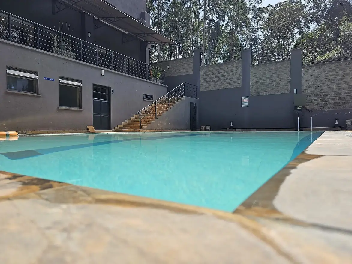 Large turquoise swimming pool with concrete deck and modern building