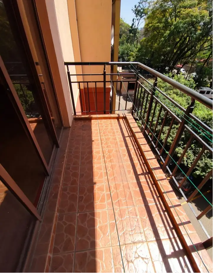 Spacious terracotta-tiled balcony with metal railings overlooking greenery