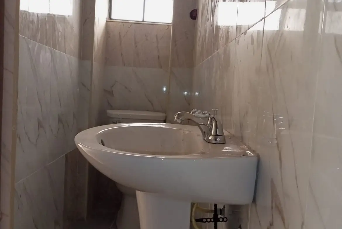 Simple bathroom with white pedestal sink and tiled walls