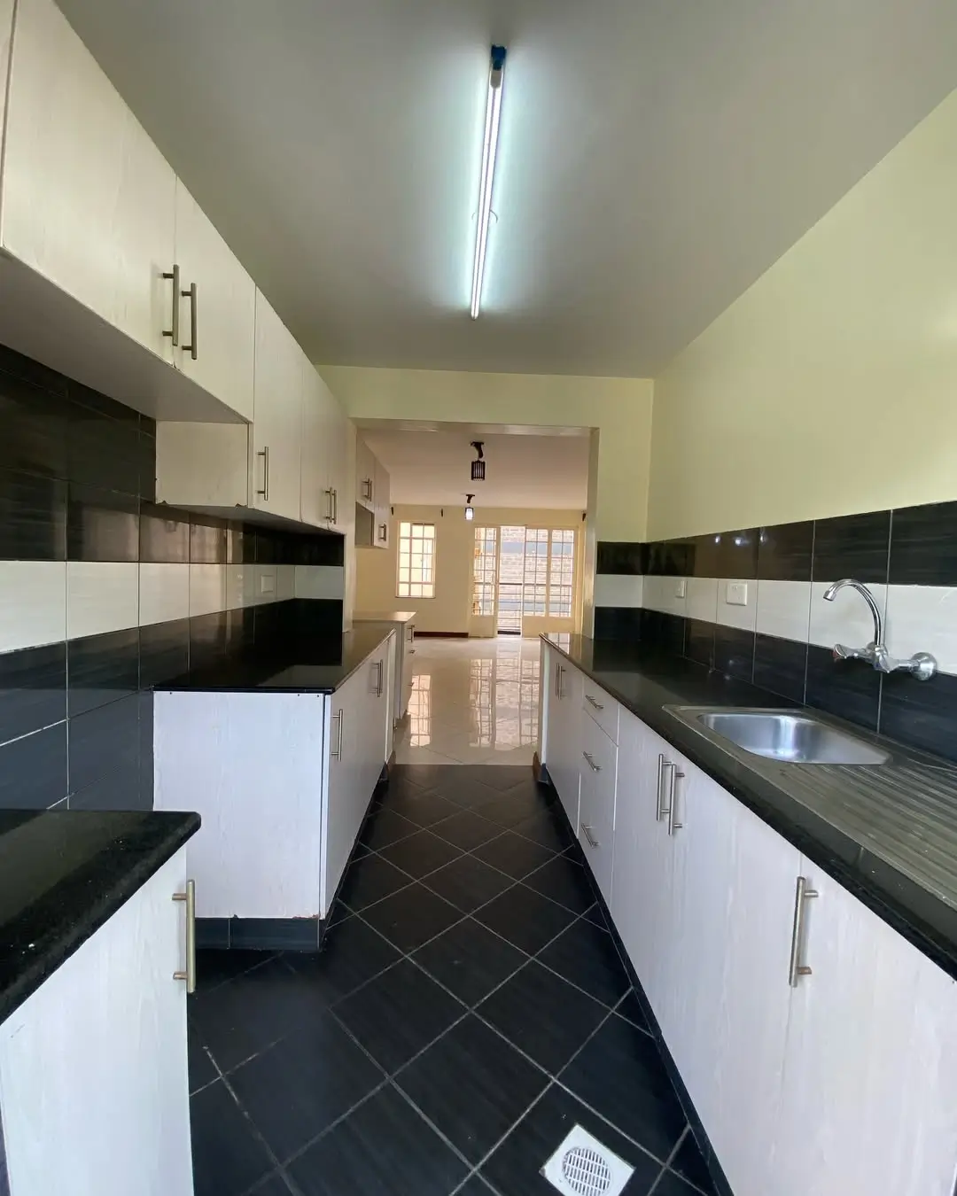Galley kitchen with white cabinetry, black countertops, and tile flooring