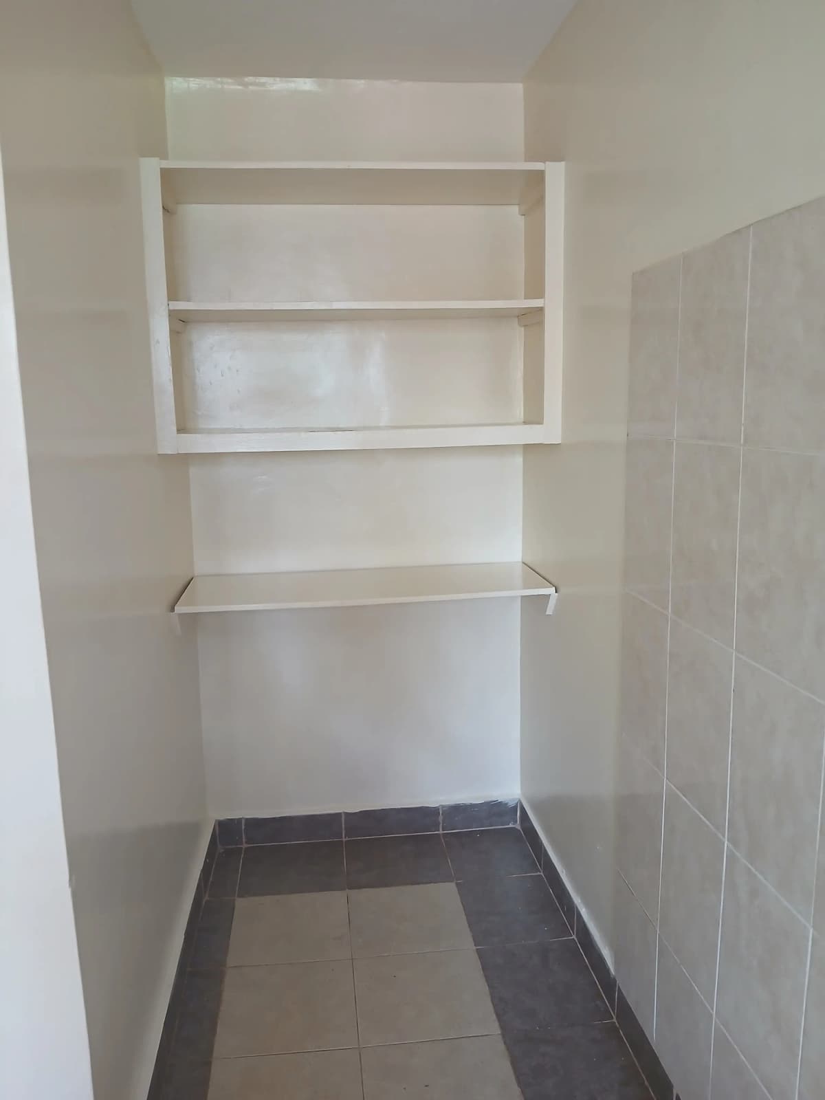 Compact pantry with open shelving and dark tile flooring