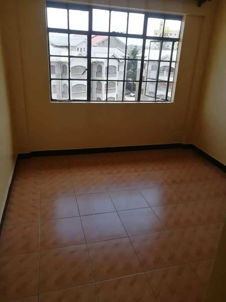 Empty bedroom with large window and terracotta tile flooring