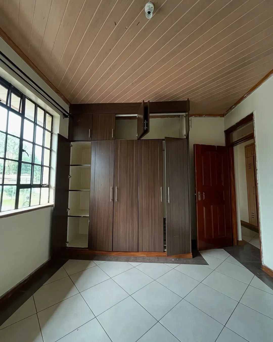 Spacious bedroom with built-in wooden wardrobes and tiled flooring