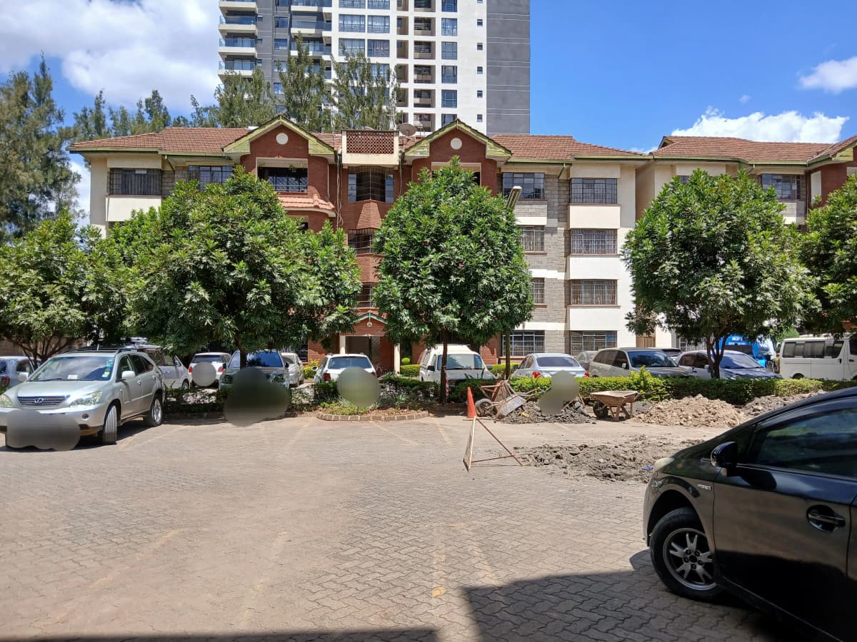Multi-story residential building with paved compound and parked vehicles