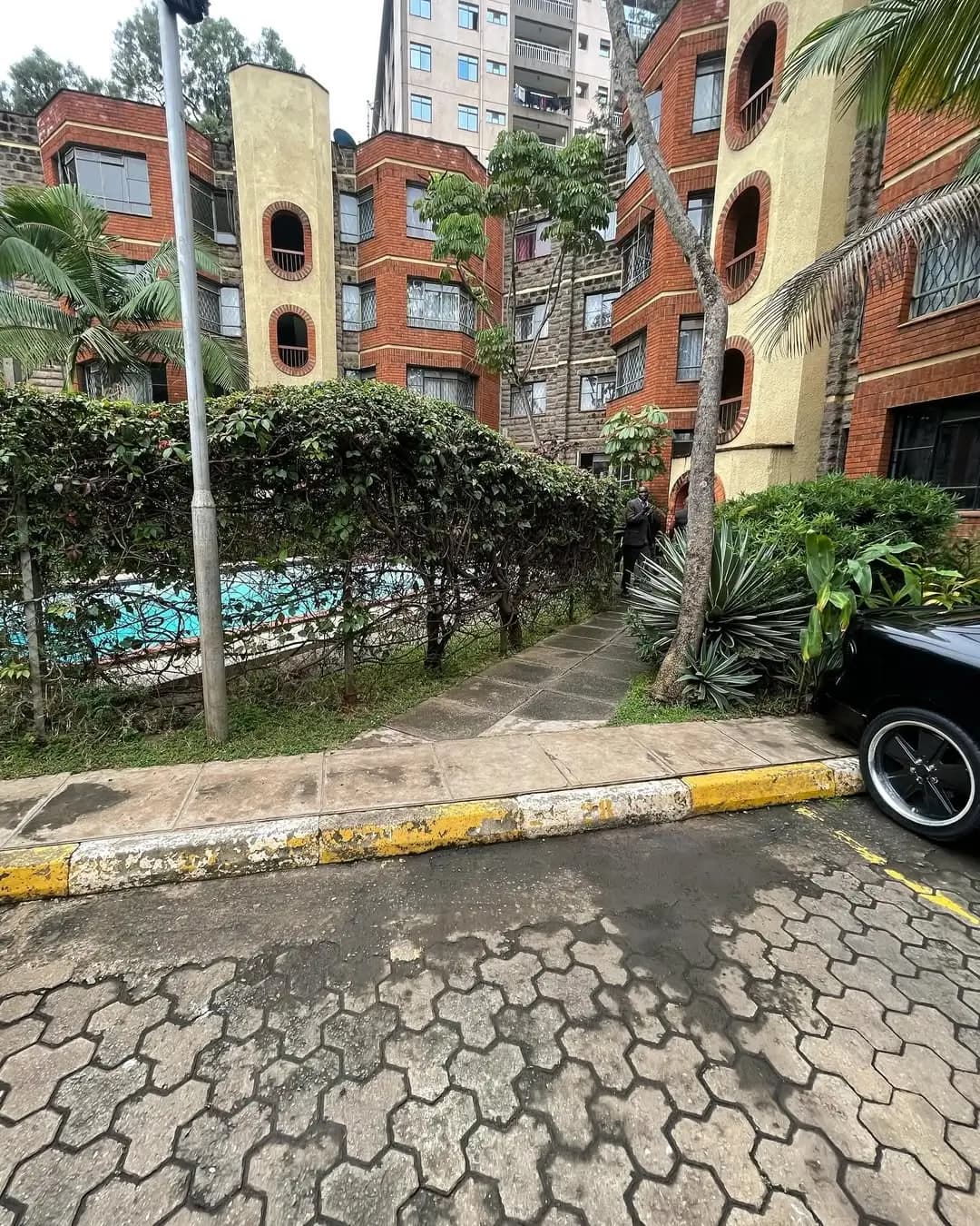 Compound entrance with brick buildings, paved driveway, tropical landscaping