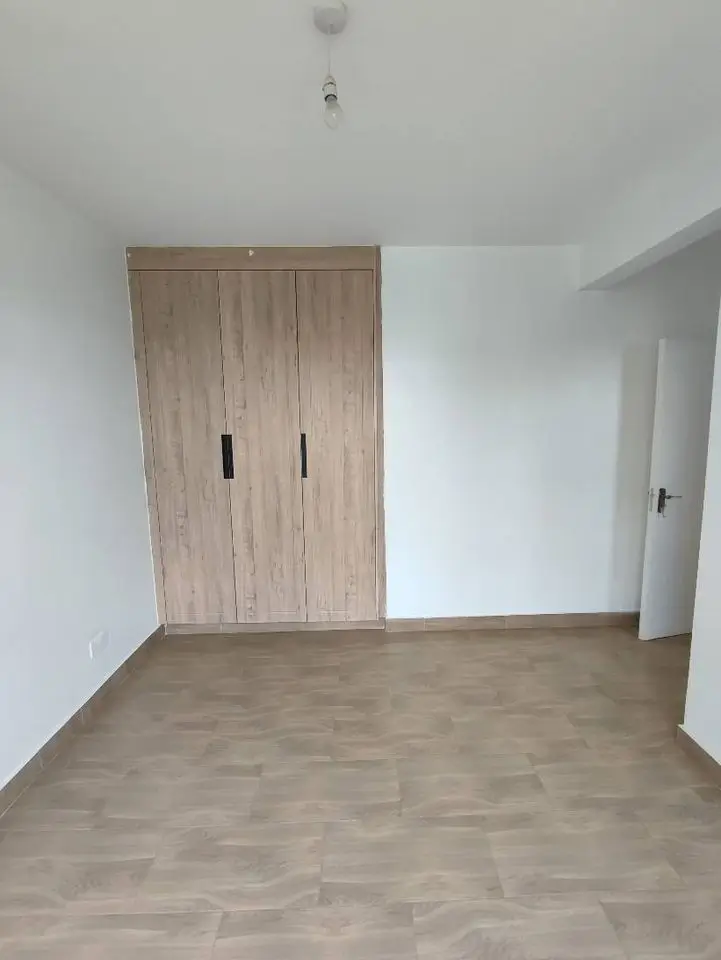 Spacious bedroom with wooden built-in wardrobes, neutral flooring