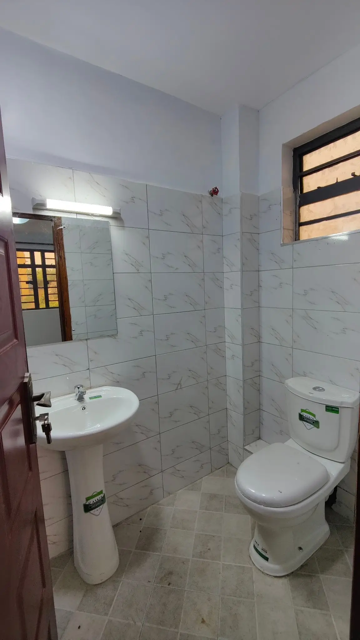 Clean bathroom with pedestal sink, toilet, and tiled walls
