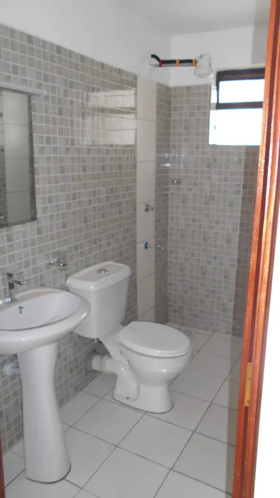 Bathroom with dual pedestal sinks, toilet, and tiled shower enclosure