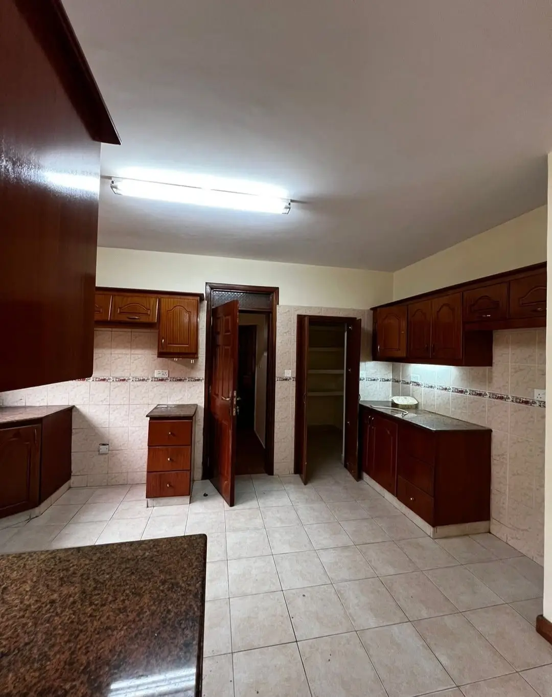Spacious kitchen with dark wood cabinets and white tile flooring