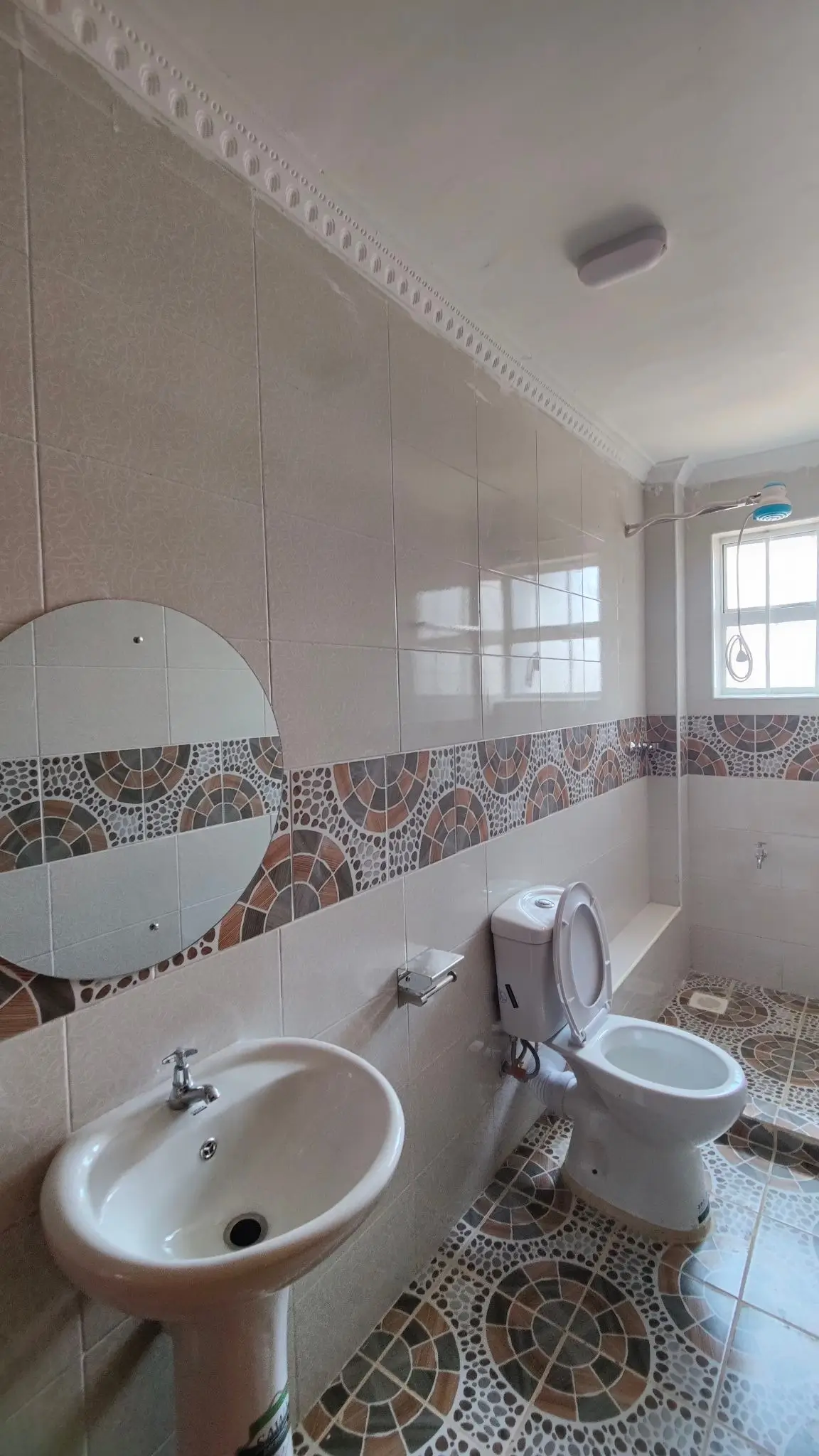 Compact bathroom with pedestal sink, toilet, and patterned tile trim