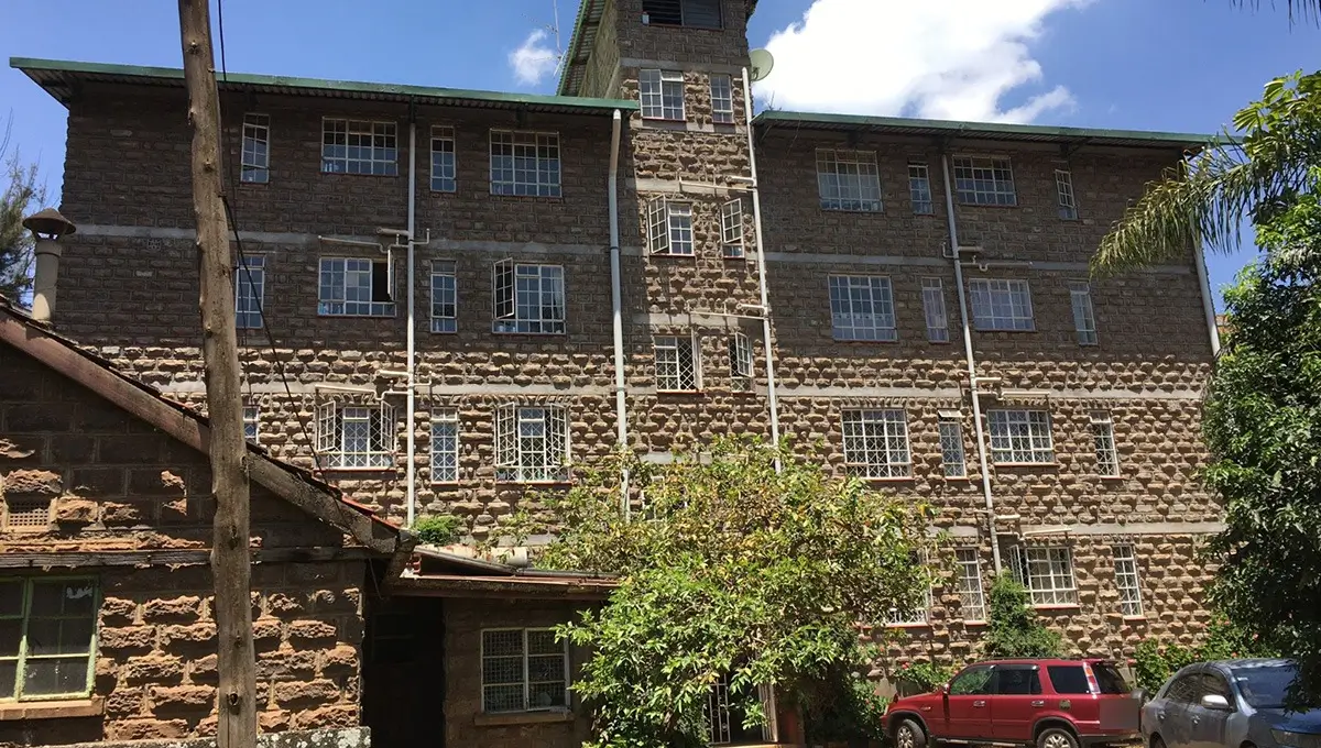 Multi-story stone building facade with ivy and parked vehicles