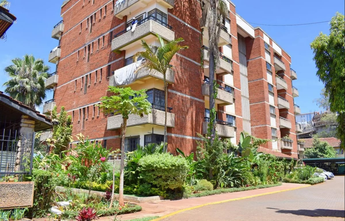 Red brick residential building with manicured grounds and palm trees