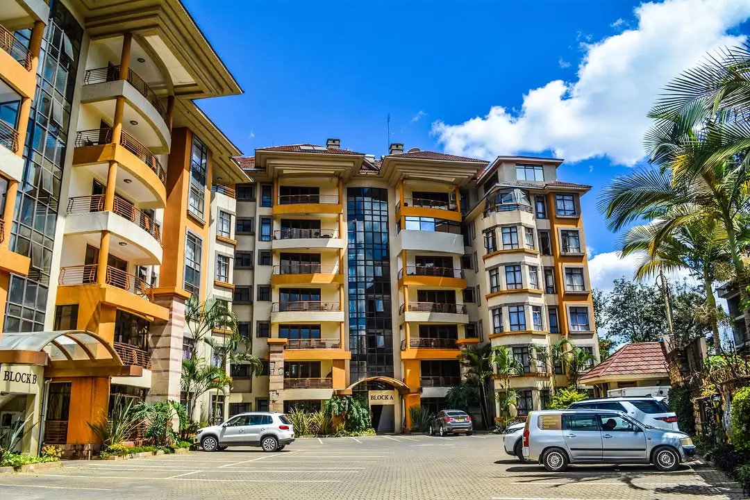 Multi-story residential complex with yellow and dark facade, landscaping