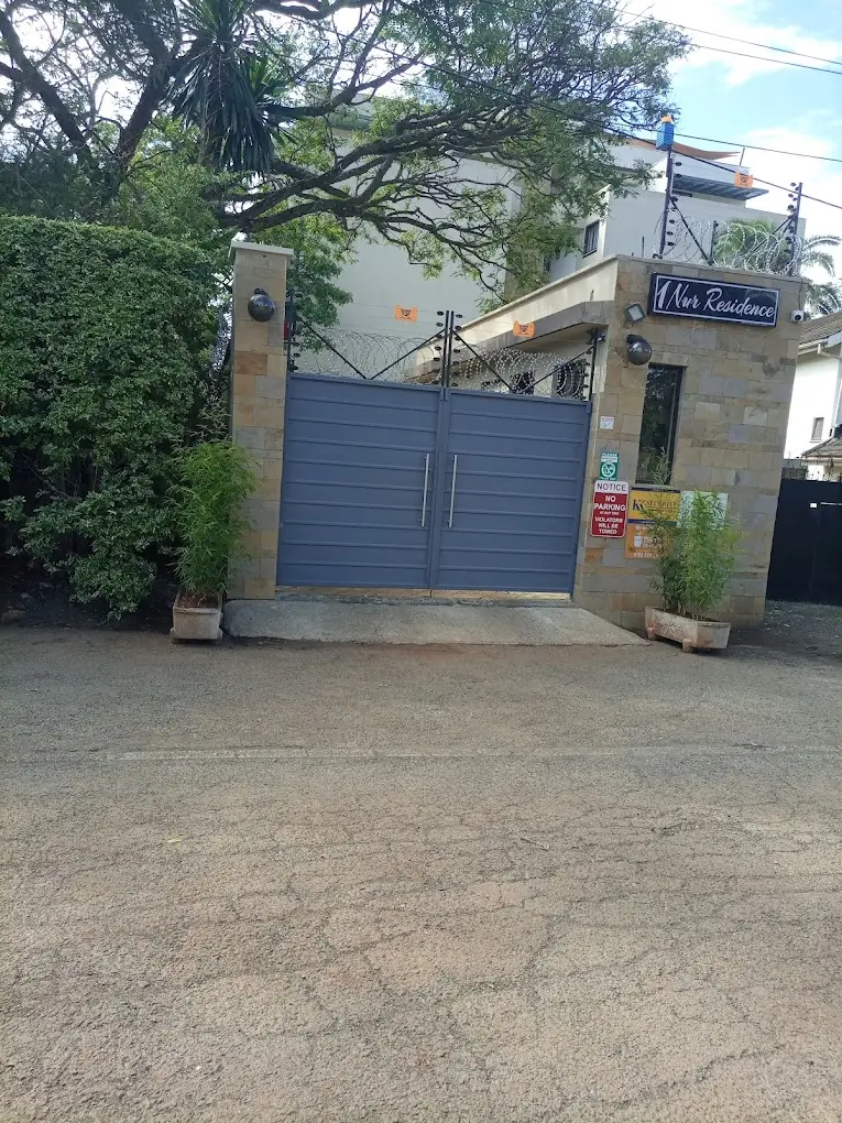 Gated compound entrance with blue double gates and mature trees