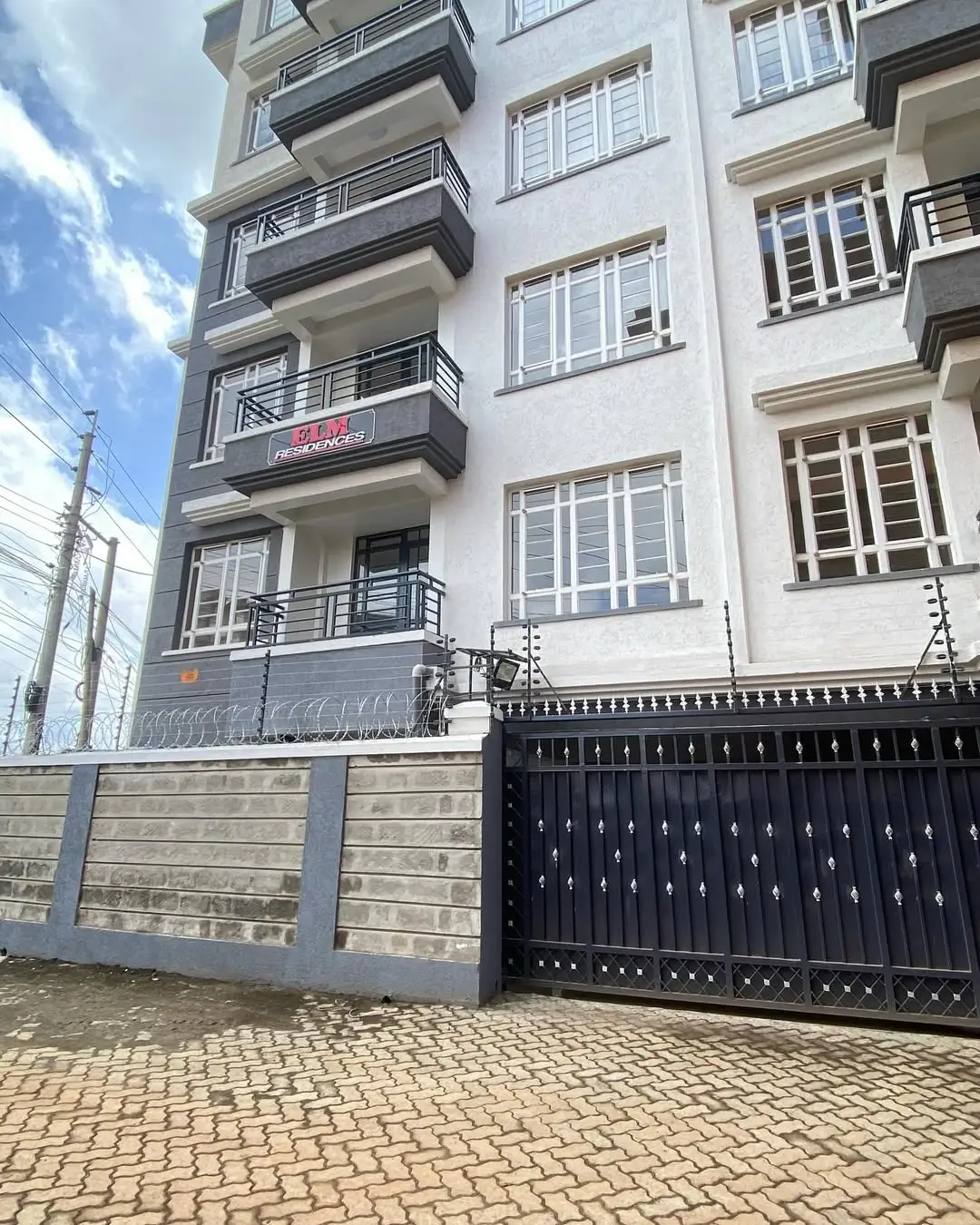Modern apartment building facade with black gate and paved driveway