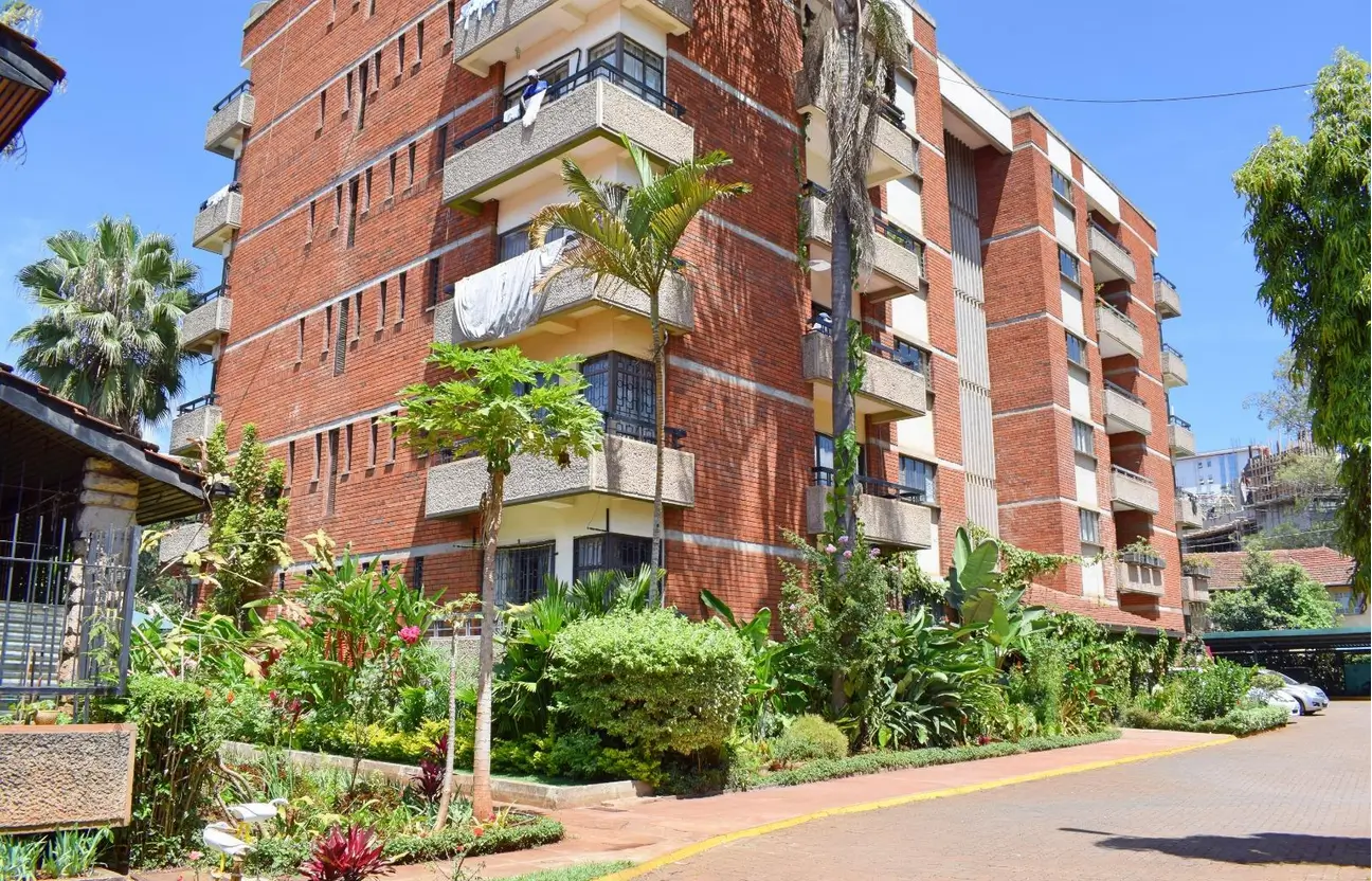 Red brick residential building with manicured grounds and palm trees