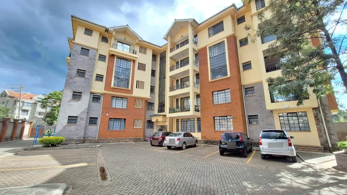 Multi-story residential building with paved compound and parked vehicles
