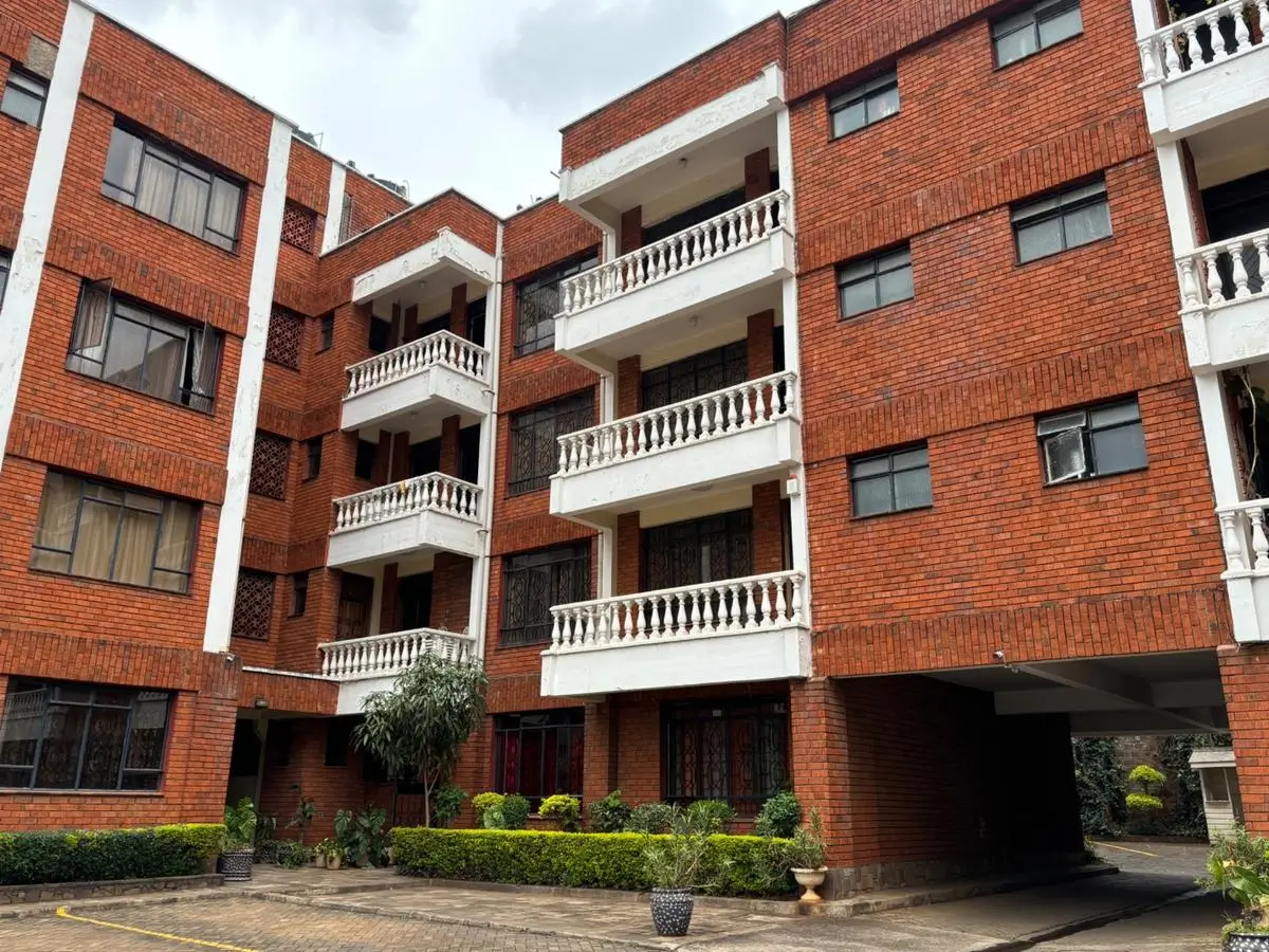 Multi-story red brick apartment building with balconies and landscaping