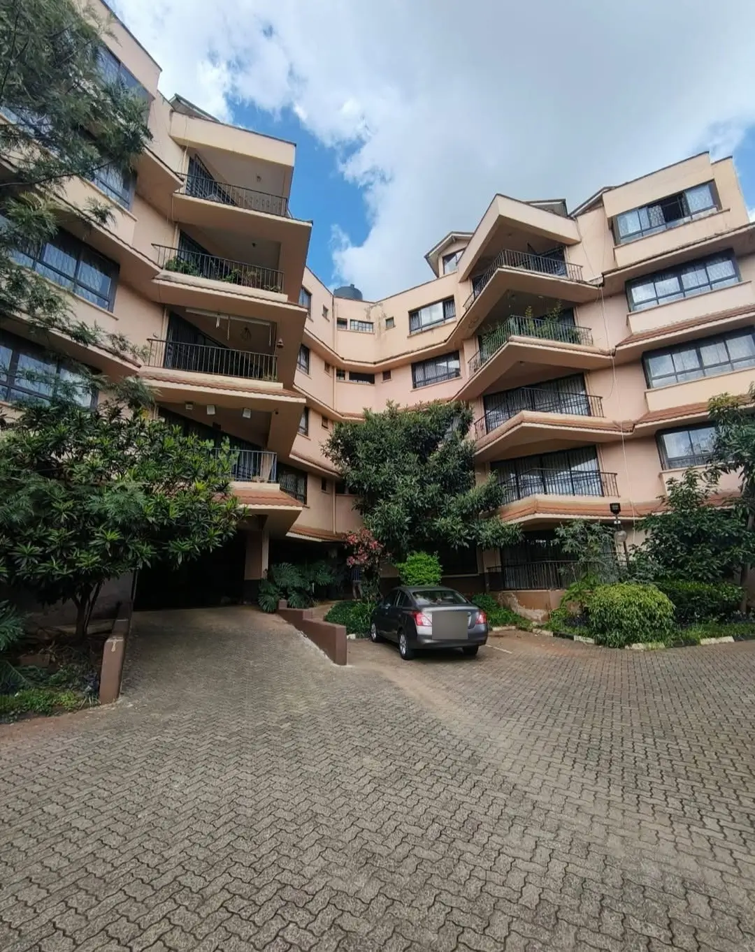 Multi-story residential building with curved balconies and parking compound