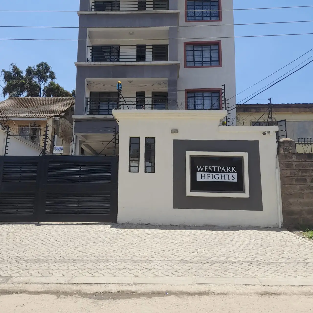 Modern multi-story apartment building with black gate and driveway