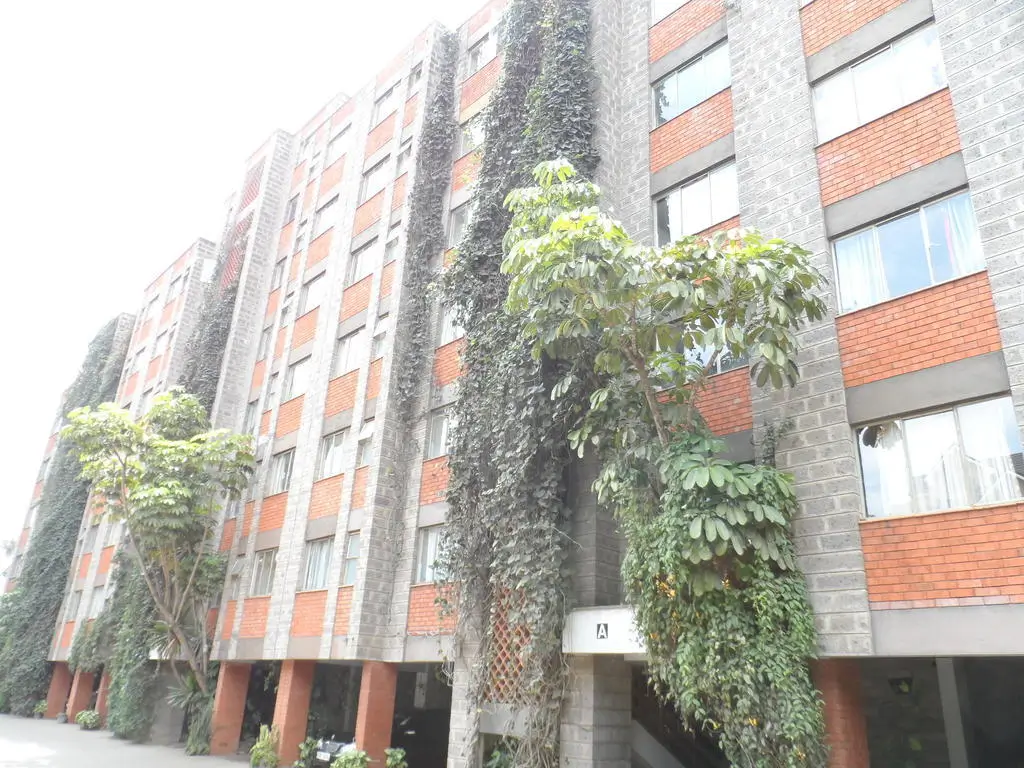 Modern multi-story brick building with ivy-covered columns and lush greenery
