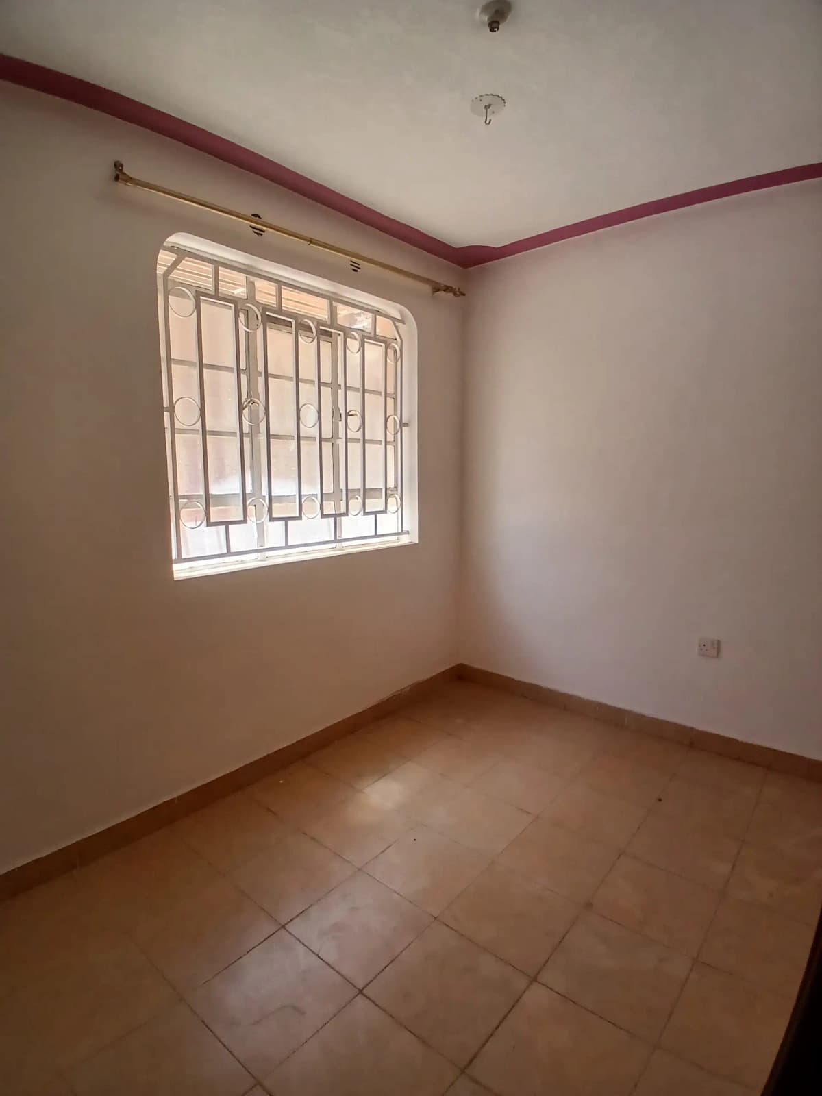 Empty bedroom with barred window and terracotta tile flooring