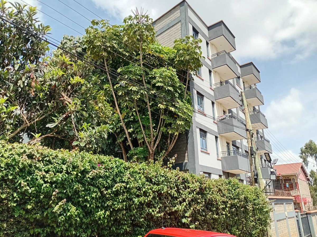 Multi-story residential building with lush green compound landscaping