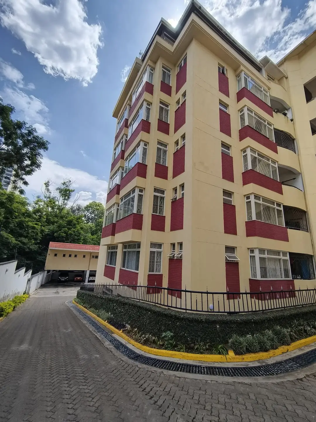 Modern apartment building with red and cream facade, gated entrance