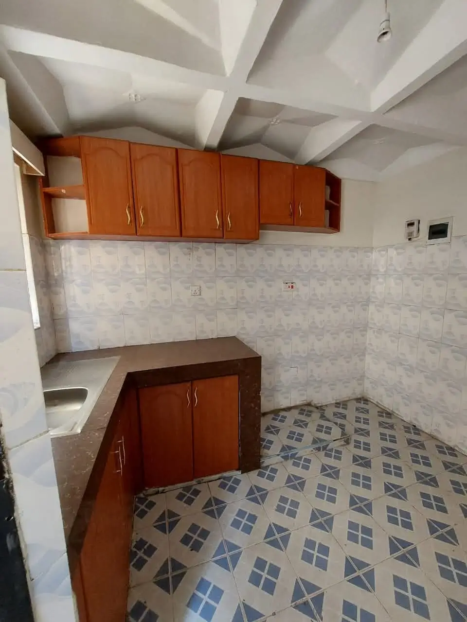 Compact kitchen with wooden cabinets and geometric floor tiles