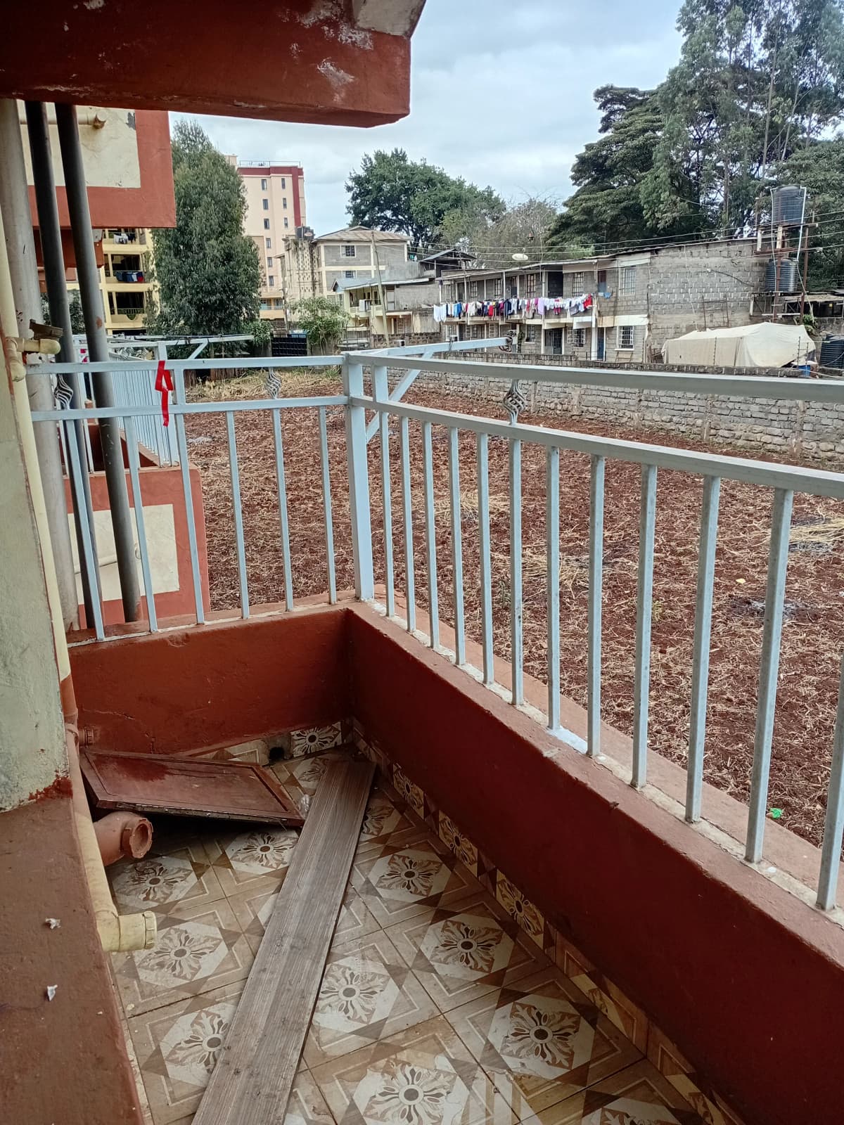 Red-painted balcony with metal railing overlooking residential neighborhood