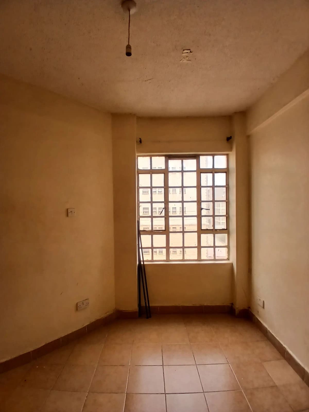 Unfurnished bedroom with barred window and terracotta tile floor