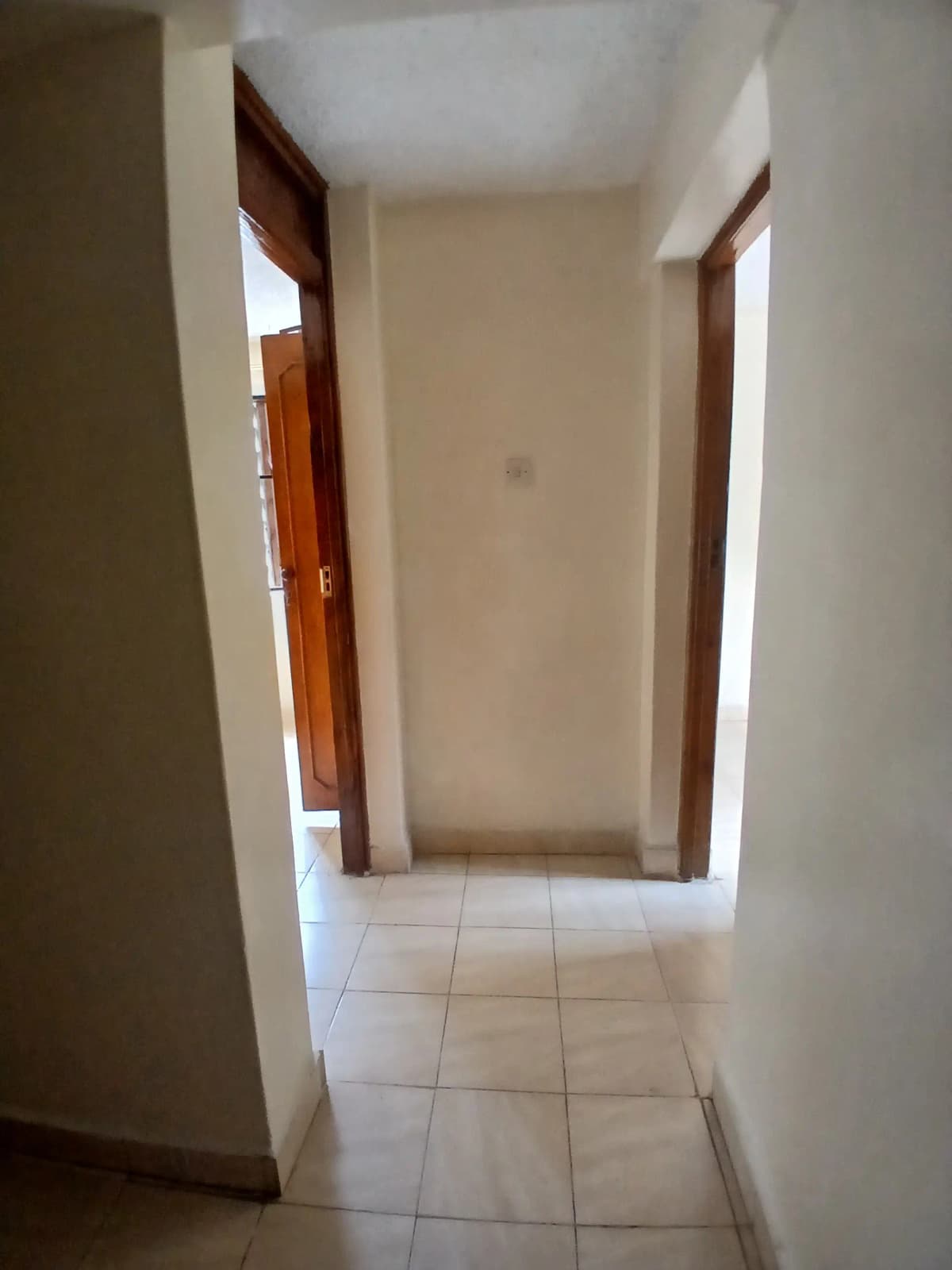 Long narrow corridor with white tile flooring and wooden doors